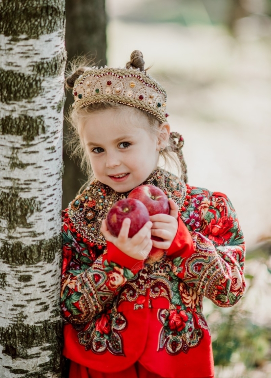 Девочка в диадеме коруне с яблоками у дерева